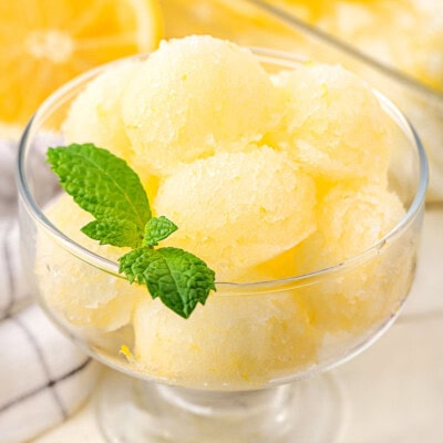 A glass bowl with lots of scoops of lemon sorbet with a mint leaf garnishing it.
