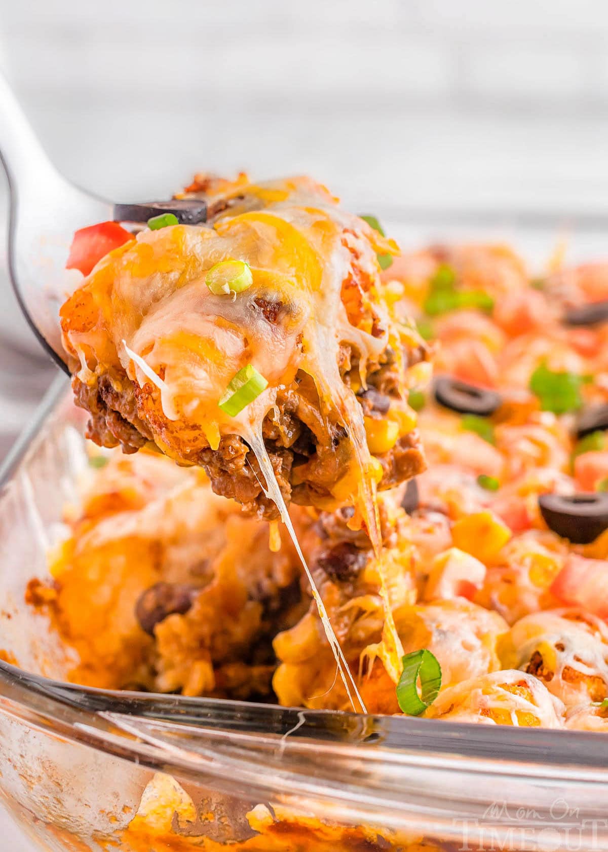 A spatula scooping a piece of mexican tater tot casserole out of a glass pan.