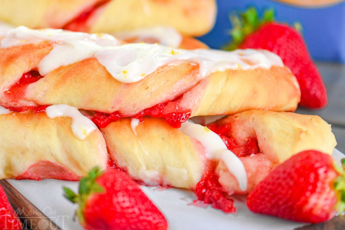 A pile of strawberry twists with strawberries placed next to them.