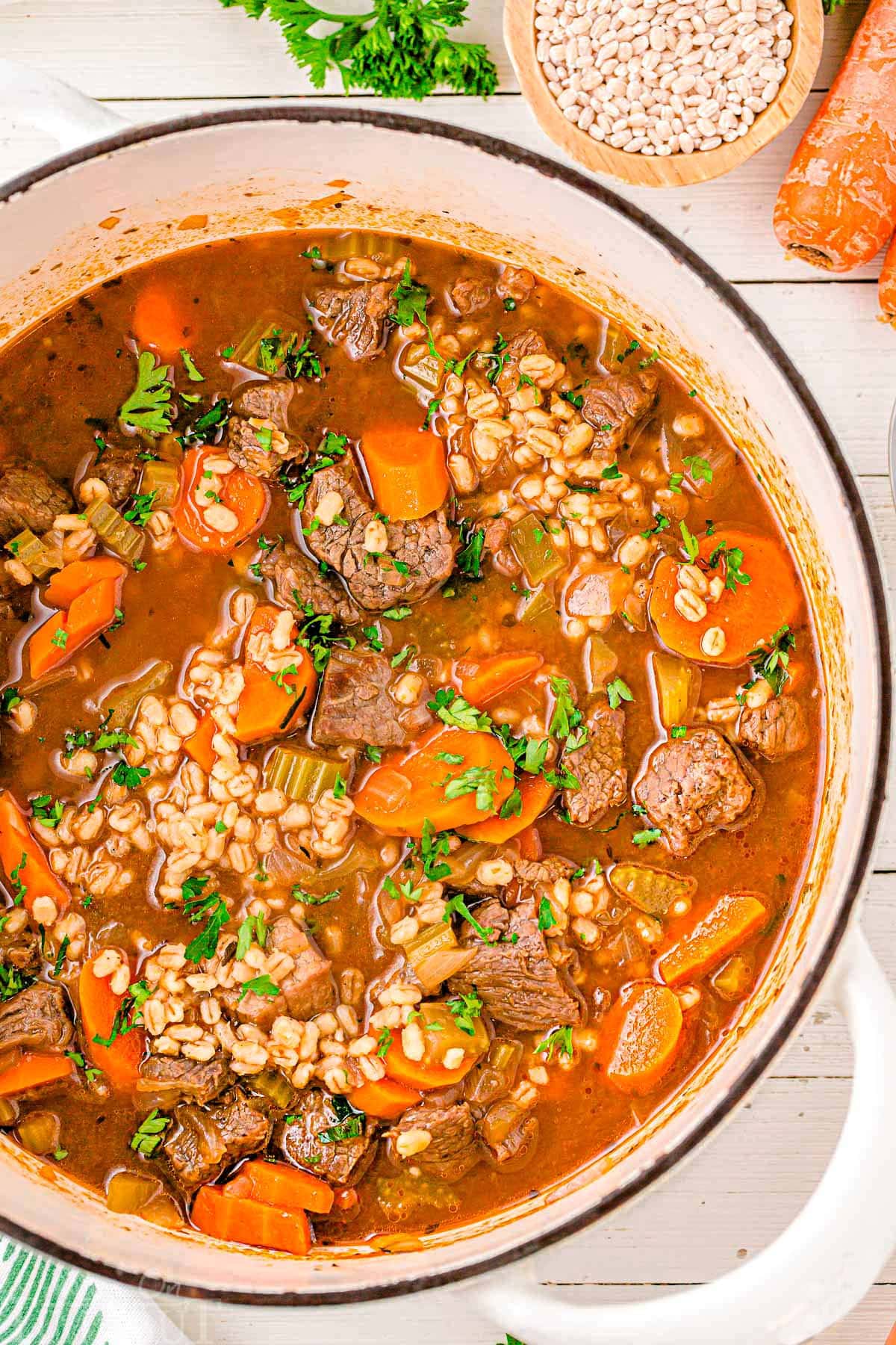 A top down shot of beef and barley soup in a white dutch oven.