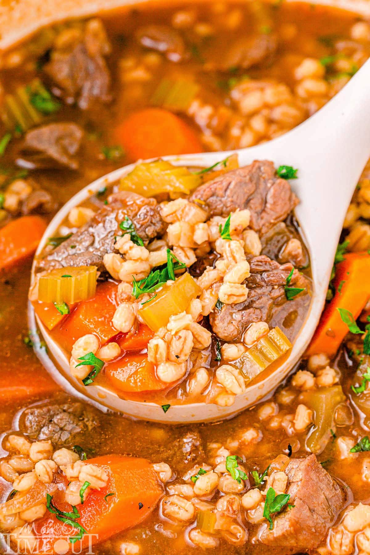 Beef Barley Soup in a dutch oven with a white ladle scooping out a serving of the soup. The soup has been garnished with fresh parsley.