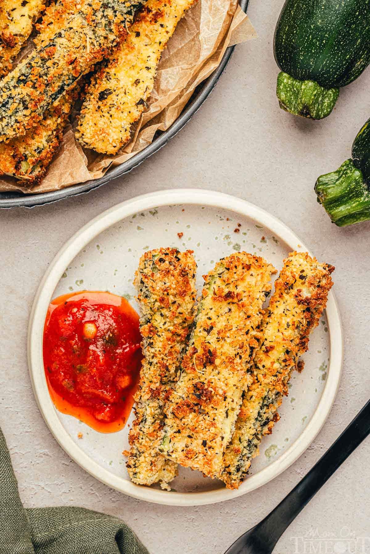 Top down view of small round white plate with three zucchini fries on it and a dollop of marinara.