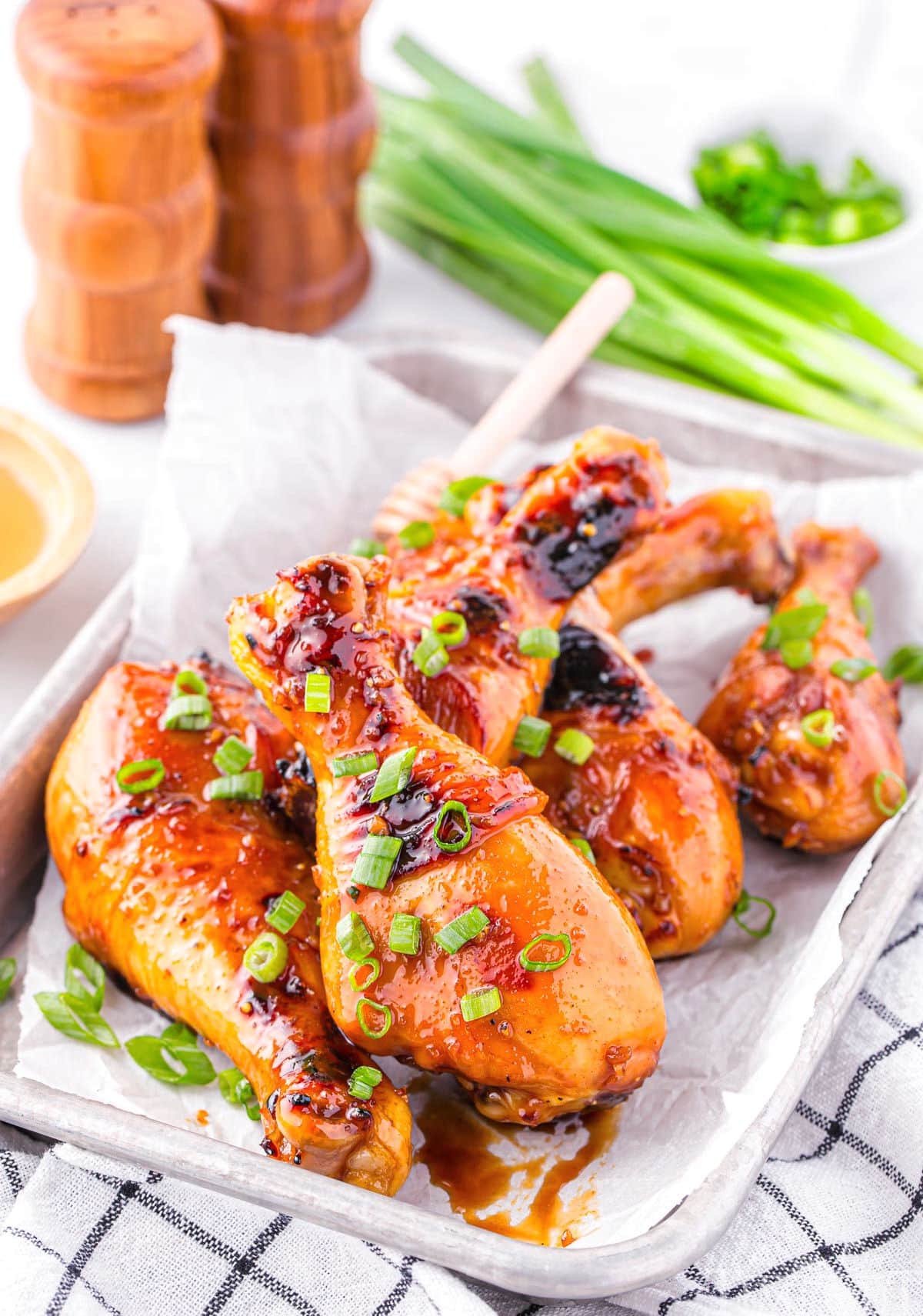 Honey glazed chicken drumsticks on a tray. Green onions can be seen in the background.