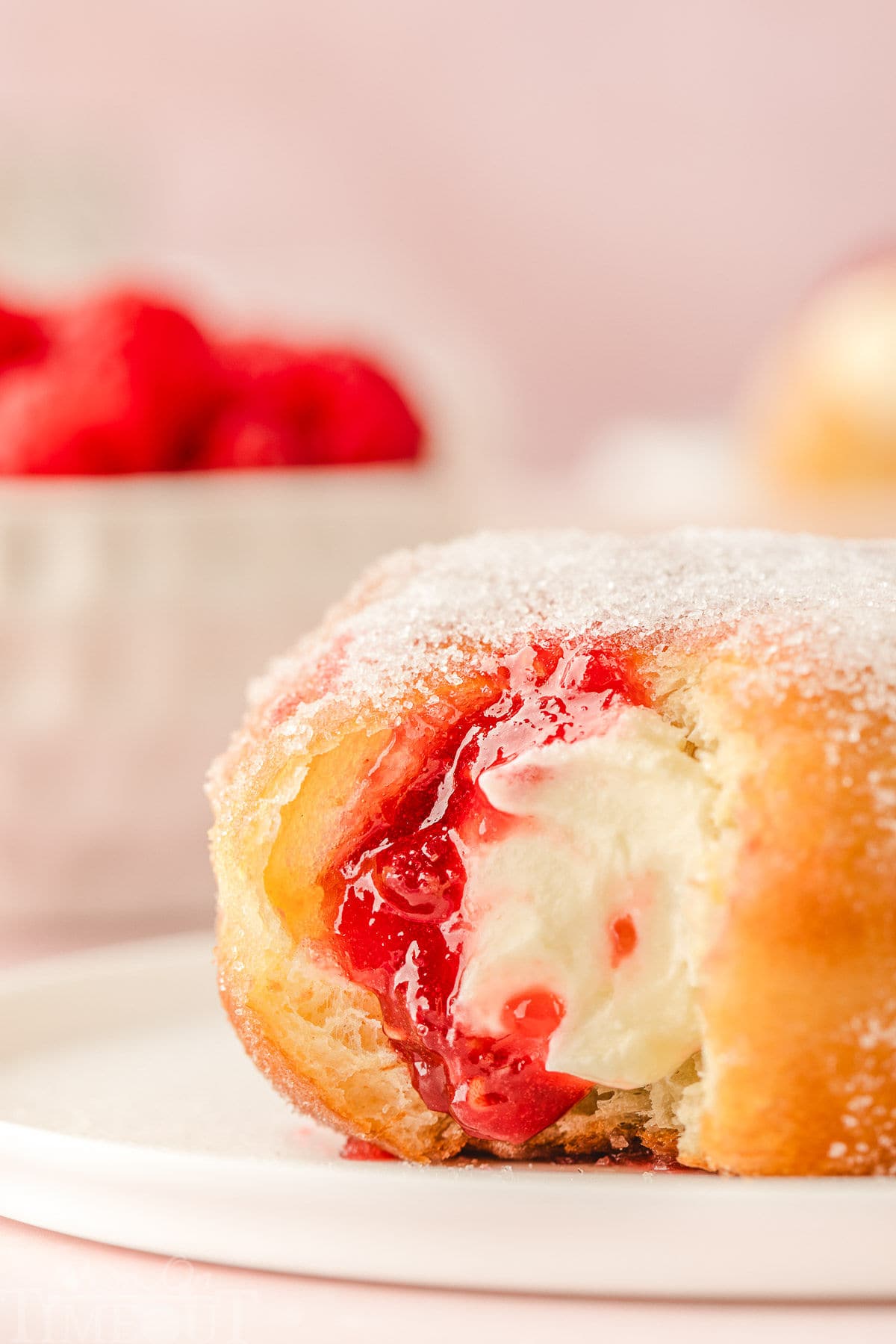 Single raspberry cheesecake stuffed donut on small round white plate with bite taken.