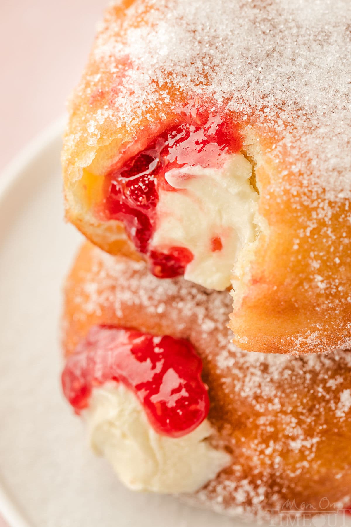 Top down angled look at two raspberry cheesecake donuts stacked on each other both with a bite taken out of it.