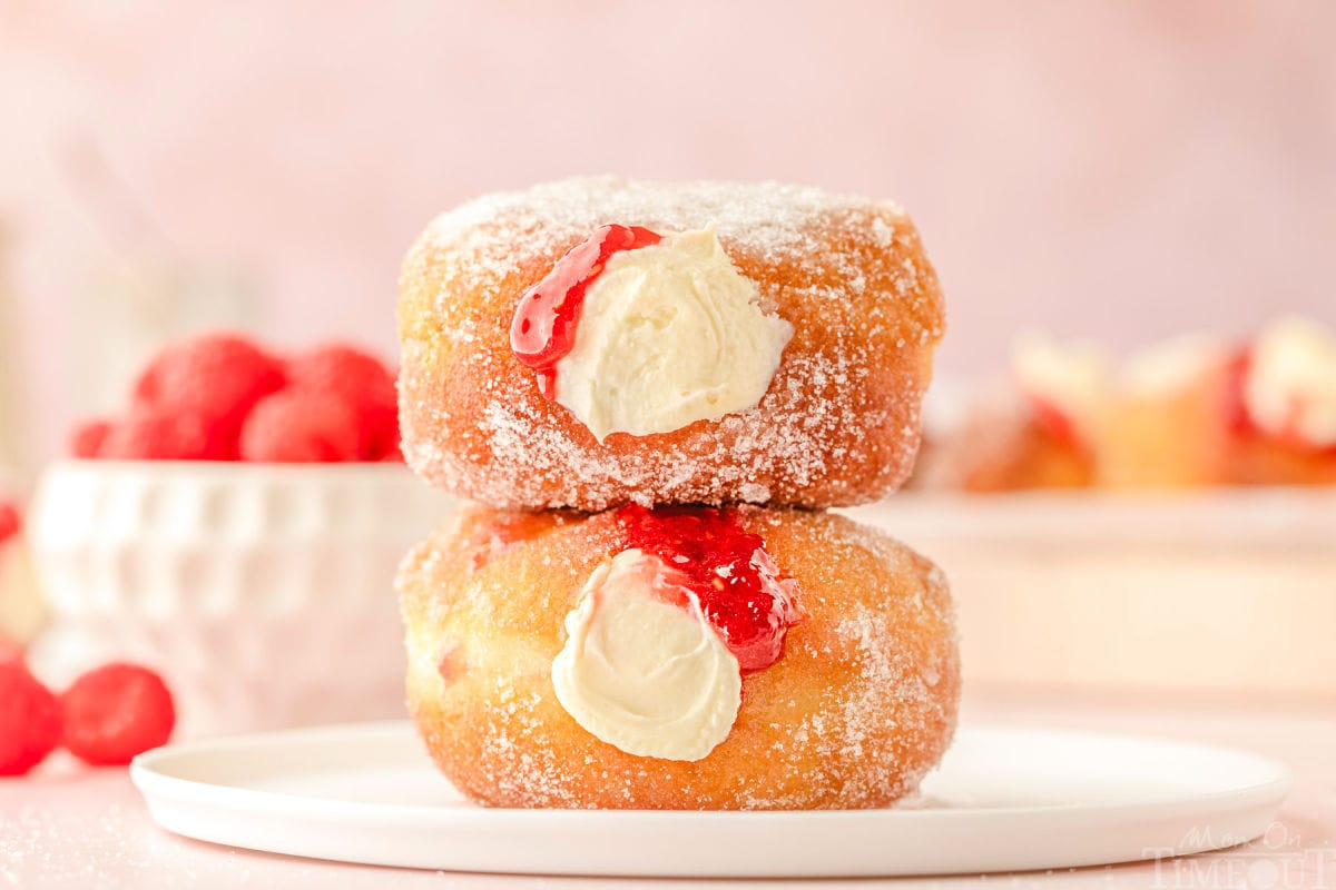 Two raspberry cheesecake stuffed donuts stacked on a round white plate.