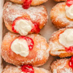 top down shot of stuffed raspberry cheesecake donuts lined up in a box. donuts have been rolled in sugar.