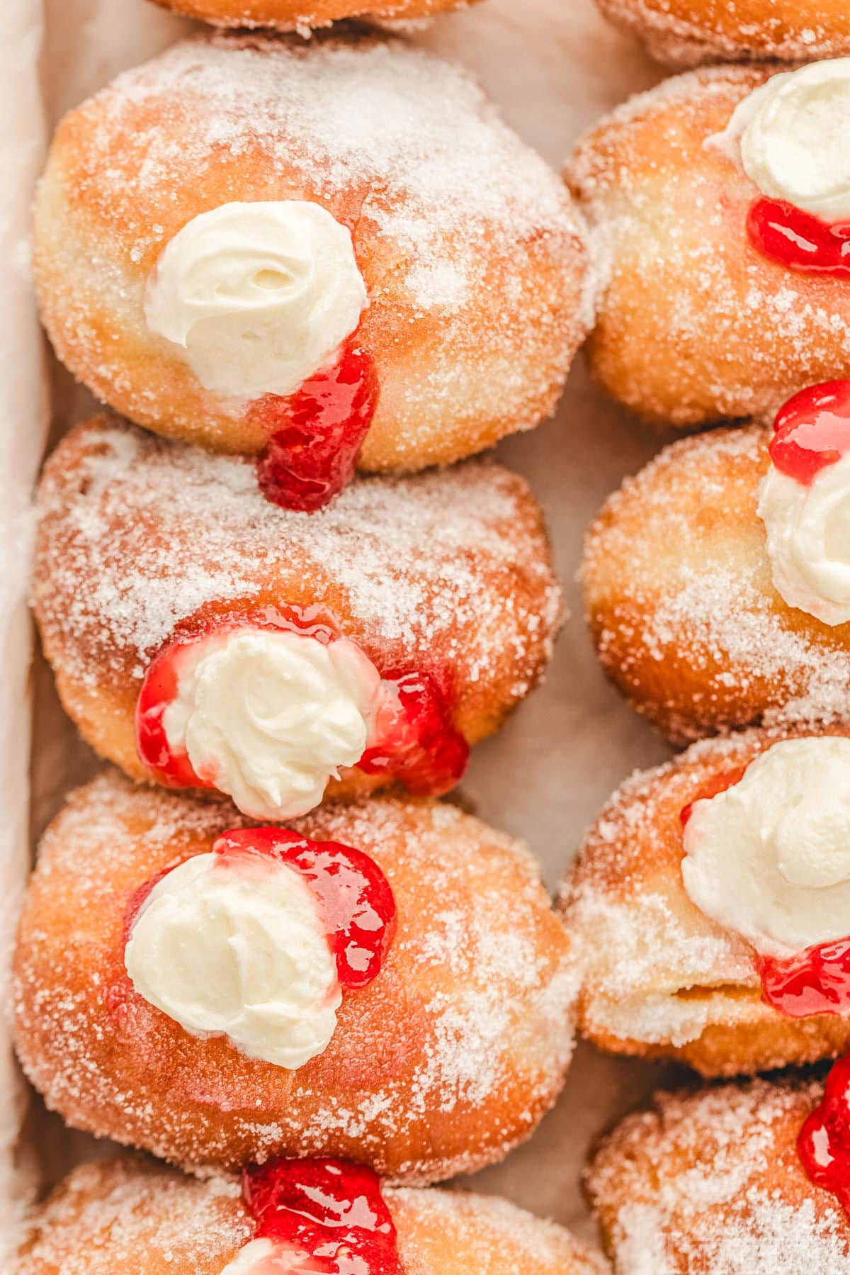 top down shot of stuffed raspberry cheesecake donuts lined up in a box. donuts have been rolled in sugar.