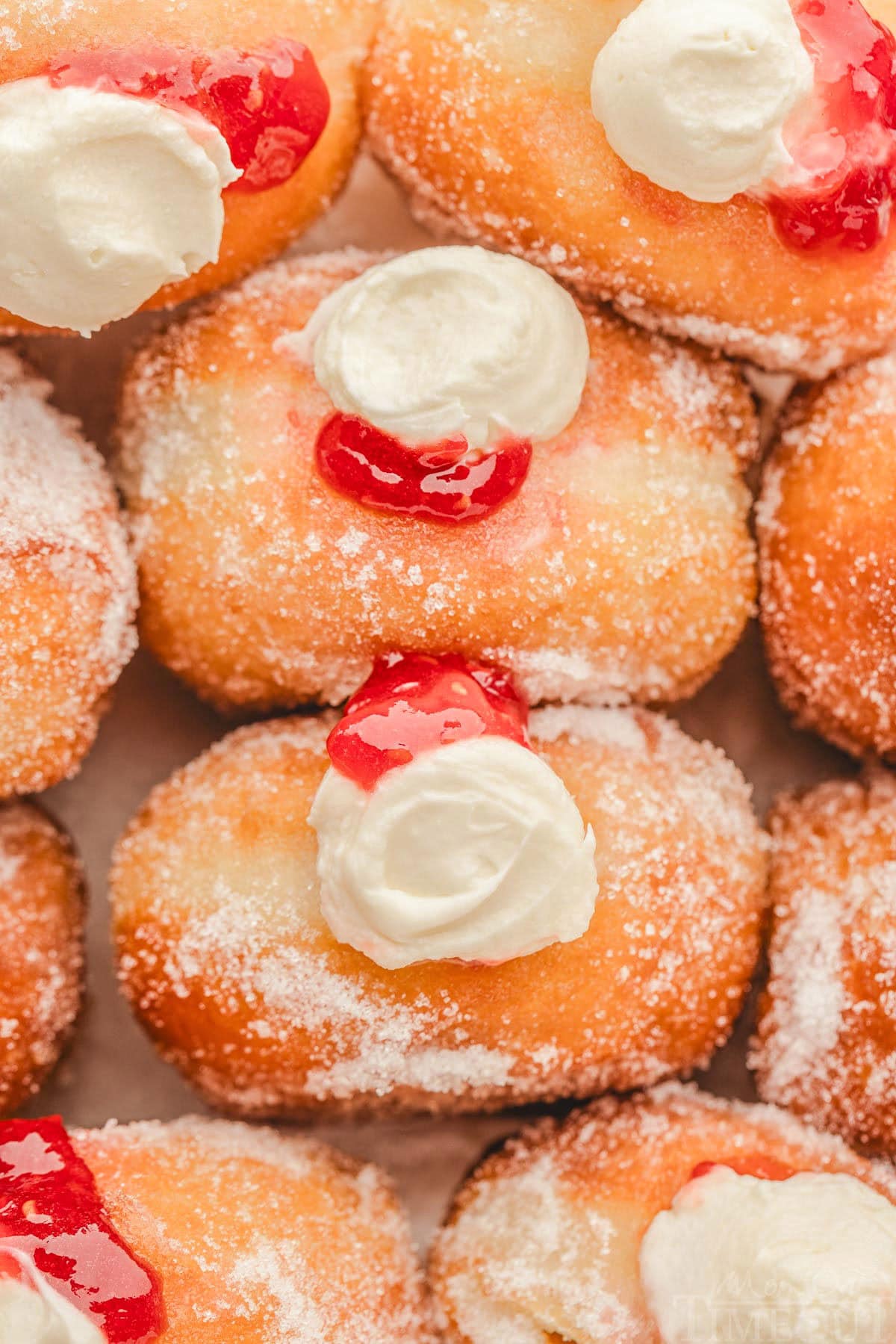 top down shot of stuffed raspberry cheesecake donuts lined up in a box. donuts have been rolled in sugar.