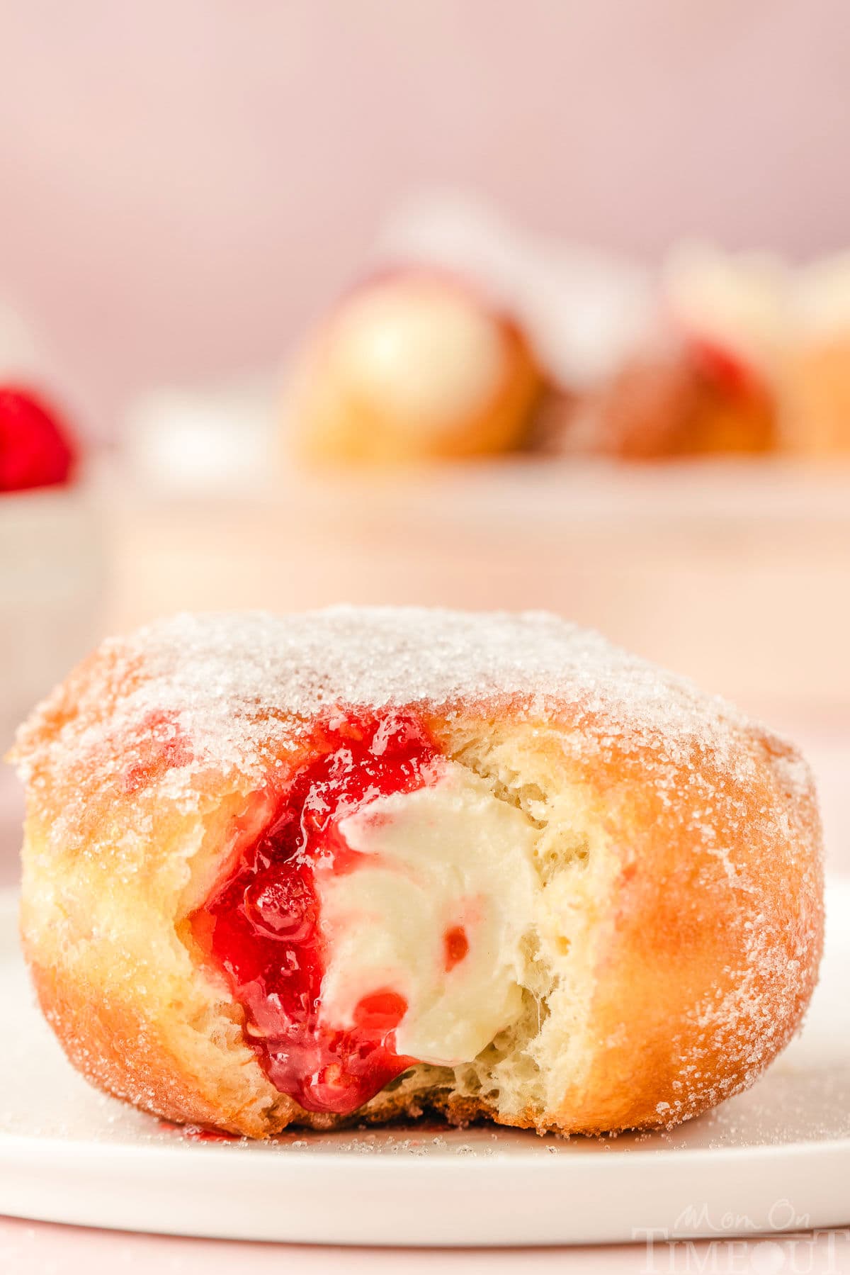 Single raspberry cheesecake stuffed donut on small round white plate with bite taken.