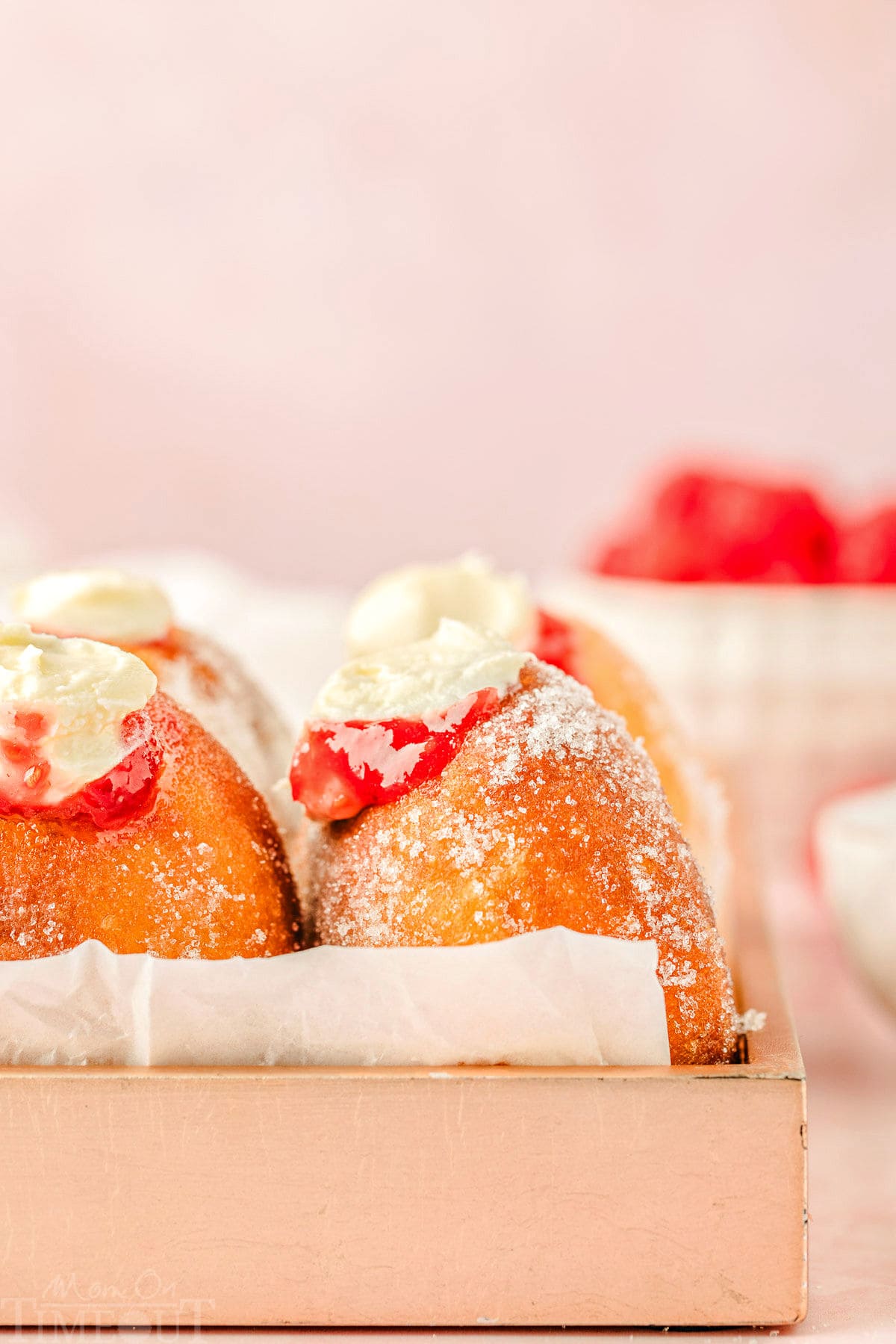 straight on shot of raspberry cheesecake donuts in a pink box. 