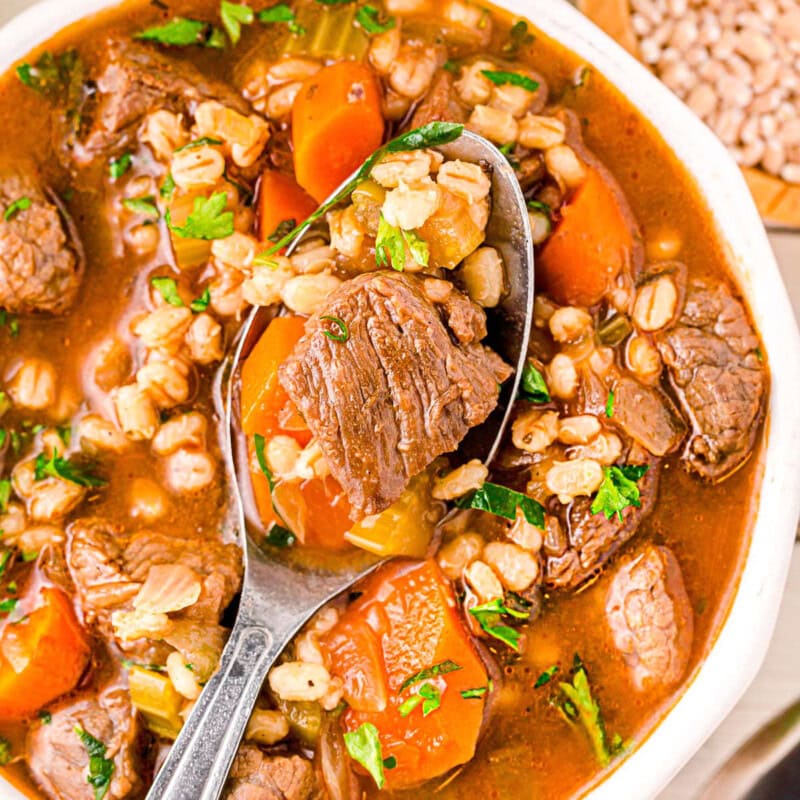 A top down view of a spoon in a bowl of beef and barley soup.