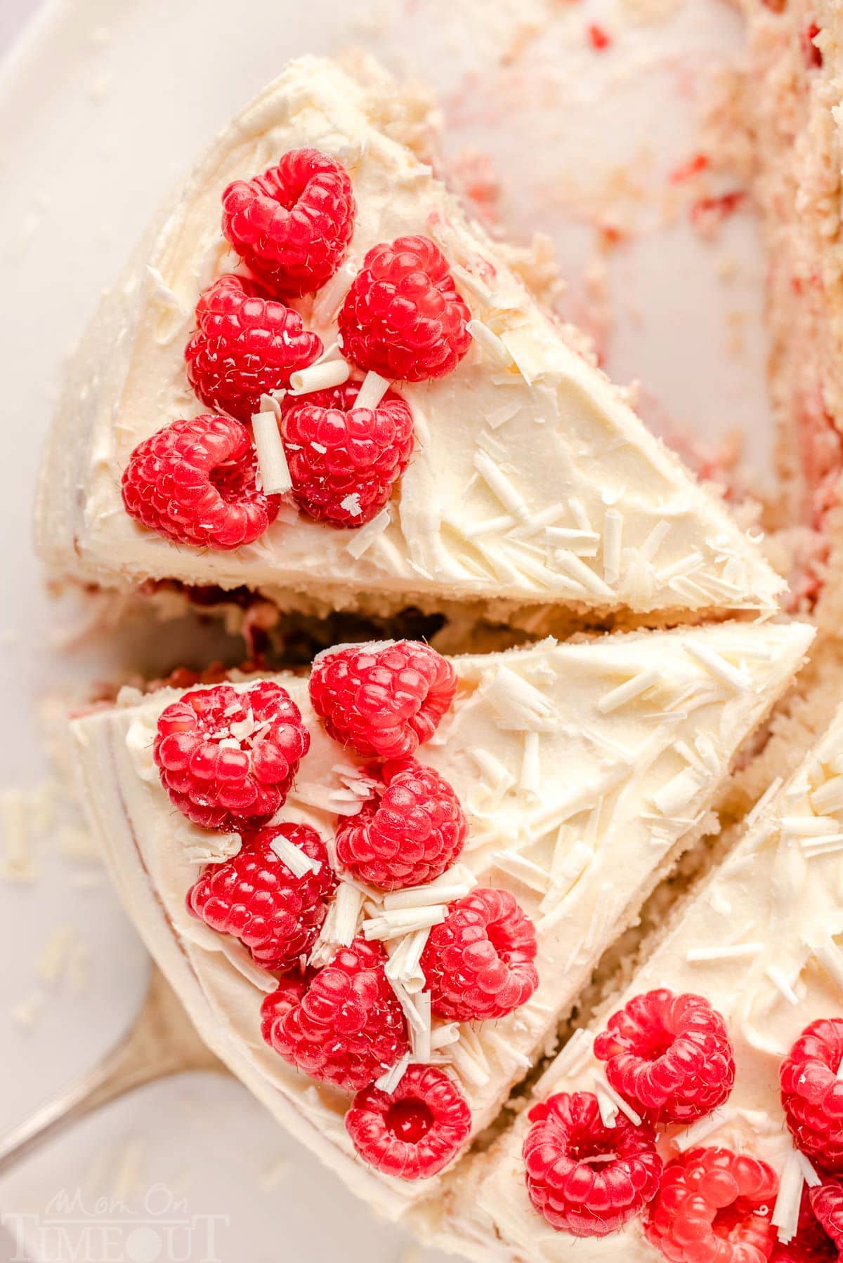 Top down look at white chocolate and raspberry cake that has been cut into generous slices. Cake is topped with red raspberries and white chocolate.