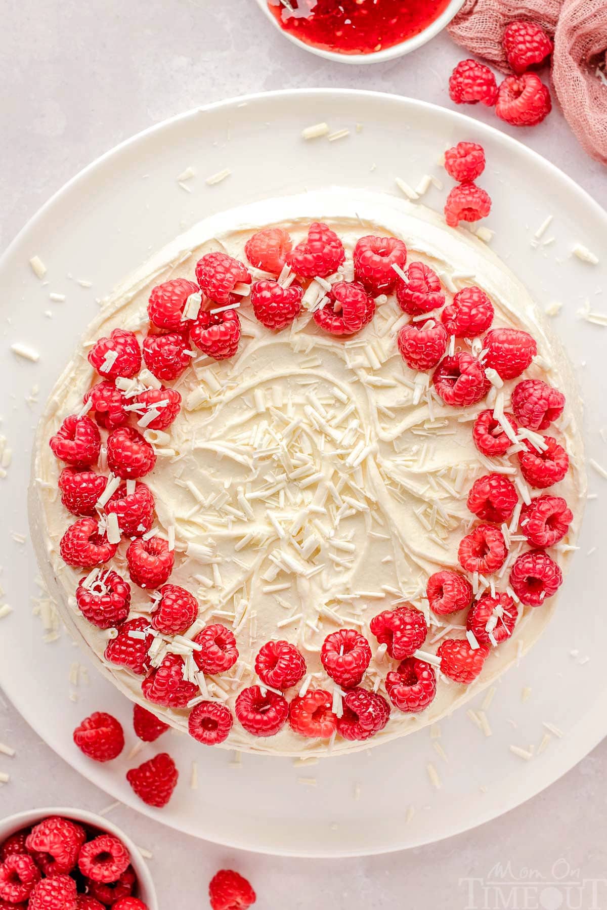 Top down view of whole white chocolate raspberry cake recipe on a large white cake plate. 