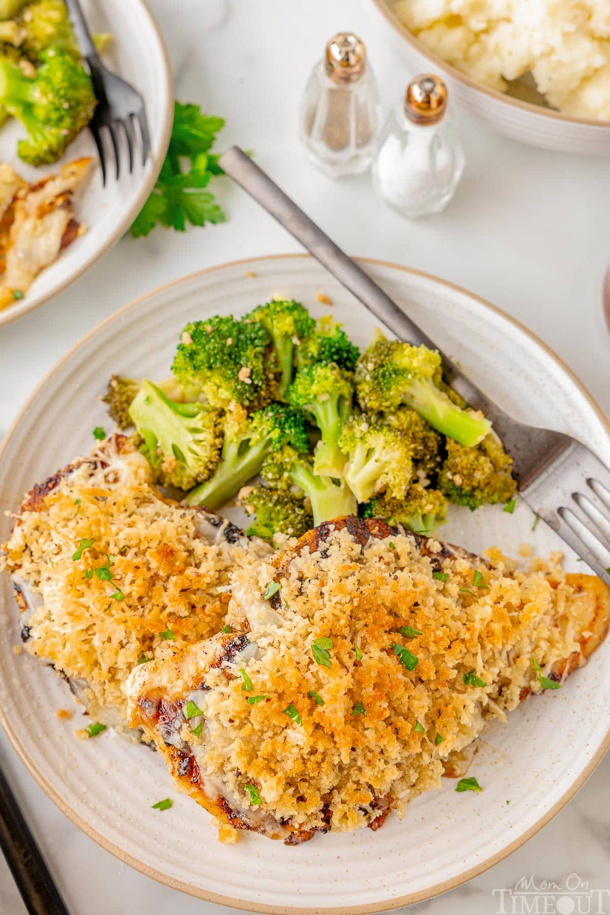 Longhorn Parmesan crusted chicken on a white plate next to a side of broccoli.