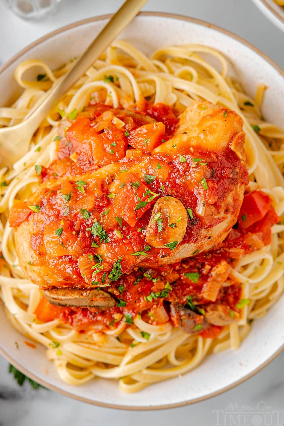 A top down shot of chicken cacciatore on a bed of pasta on a white plate.