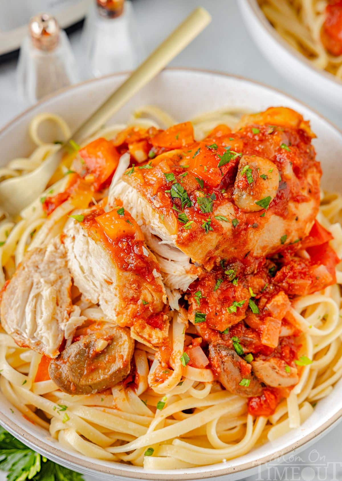 A top down shot of chicken cacciatore sliced into pieces on a bed of pasta on a white plate.