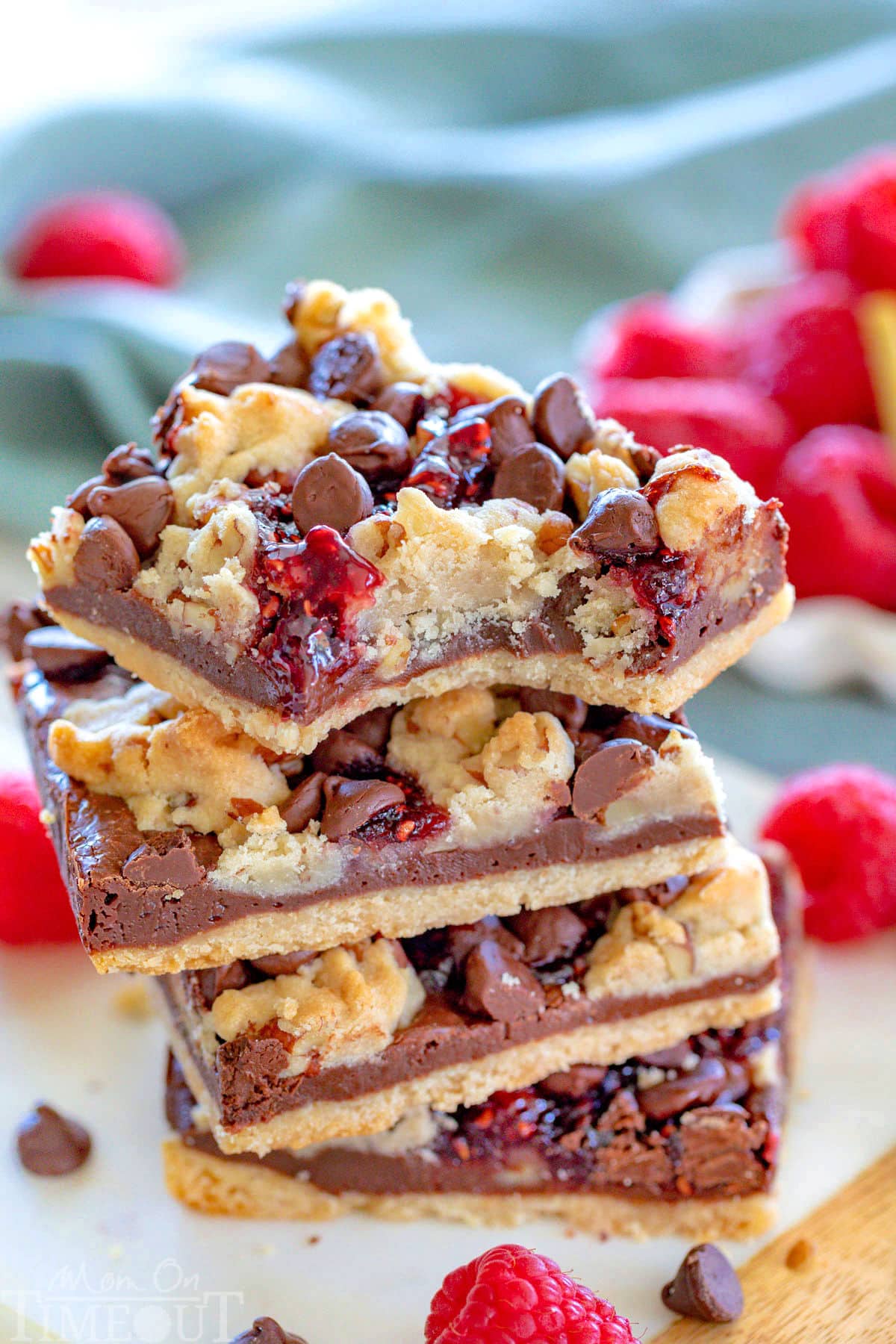 Four raspberry chocolate crumble bars stacked on small marble board with fresh raspberries in background.