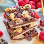 Three chocolate raspberry crumb bars stacked on a white marble board. Fresh raspberries can be seen in a white bowl in the background.