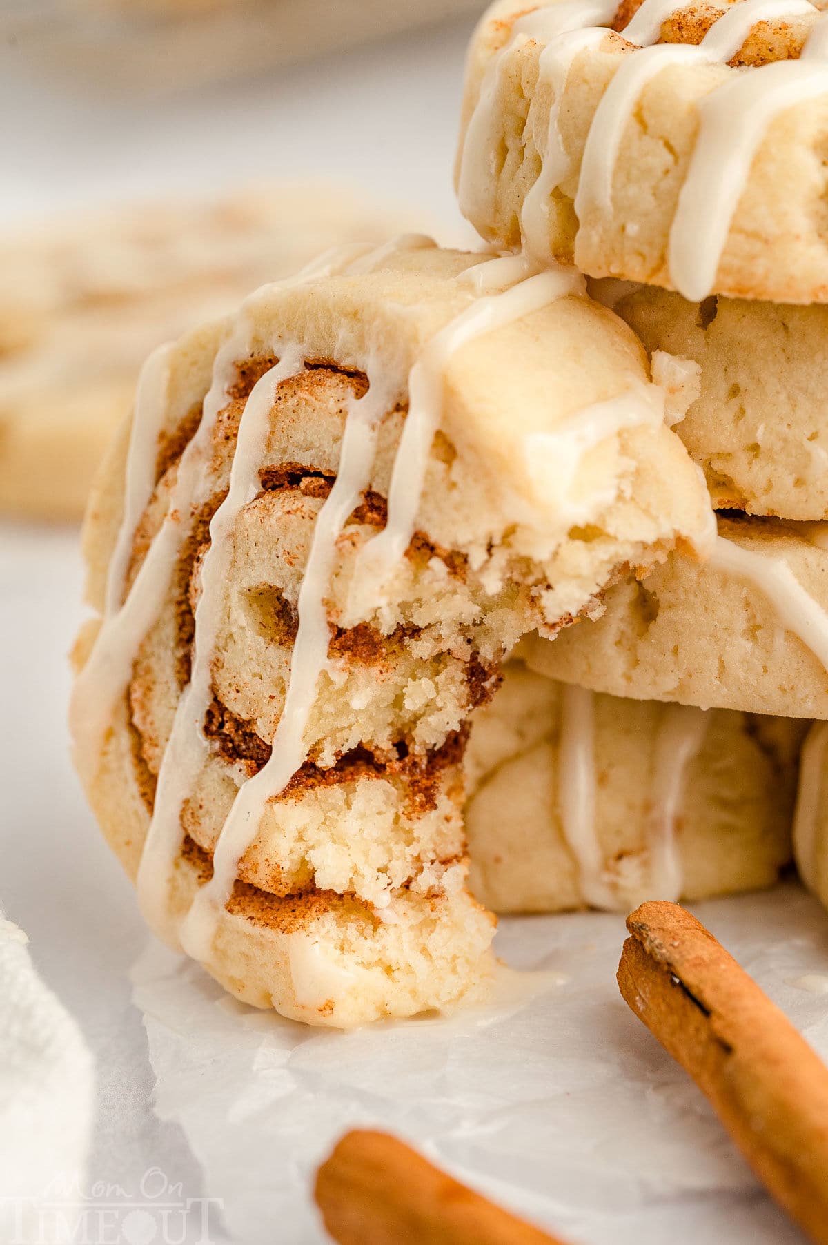 A shot of a cinnamon roll cookie with a bite take out of it leaning against a stack of more cinnamon roll cookies.