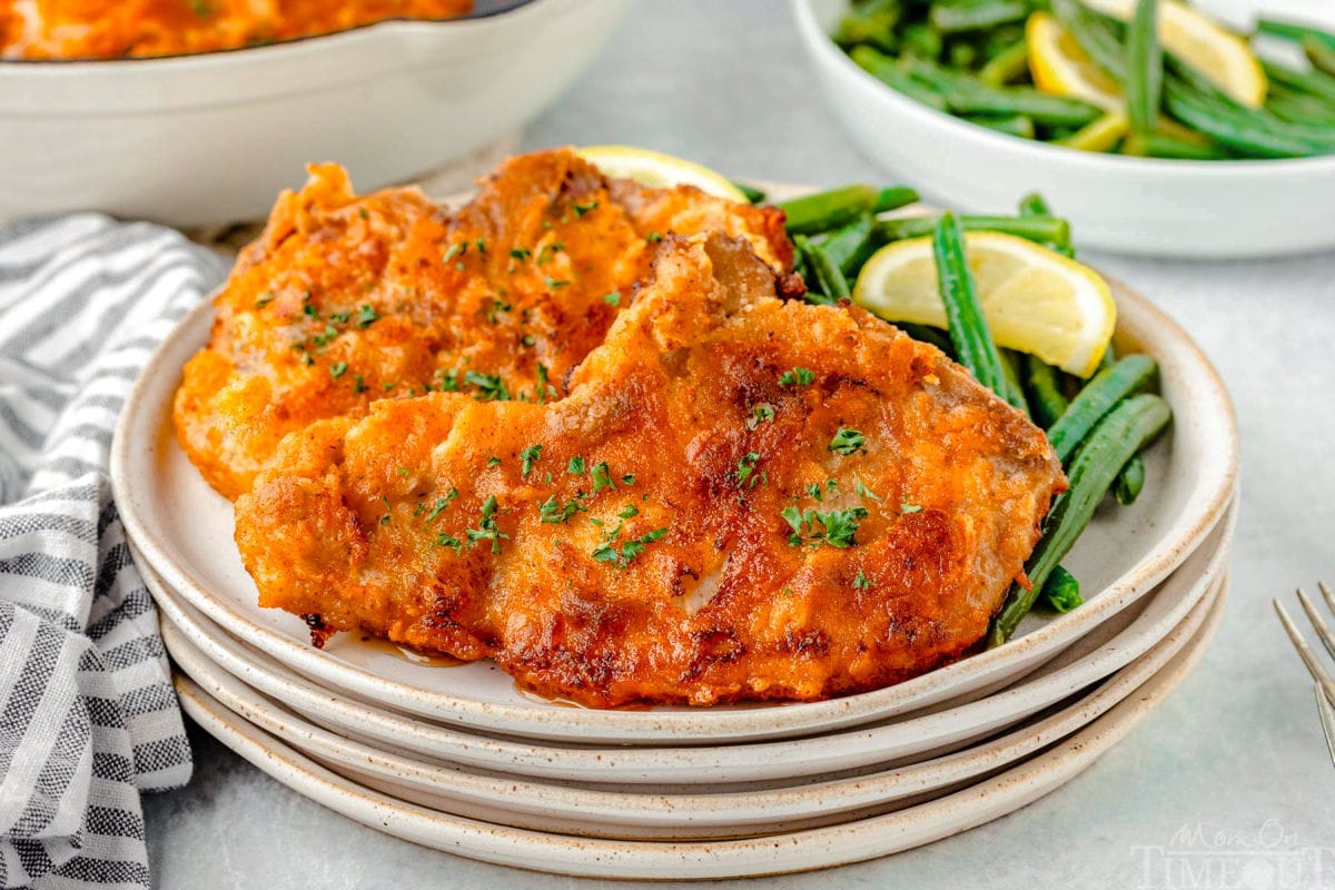 Wide shot of two fried pork chops on a stack of plate with green beans.