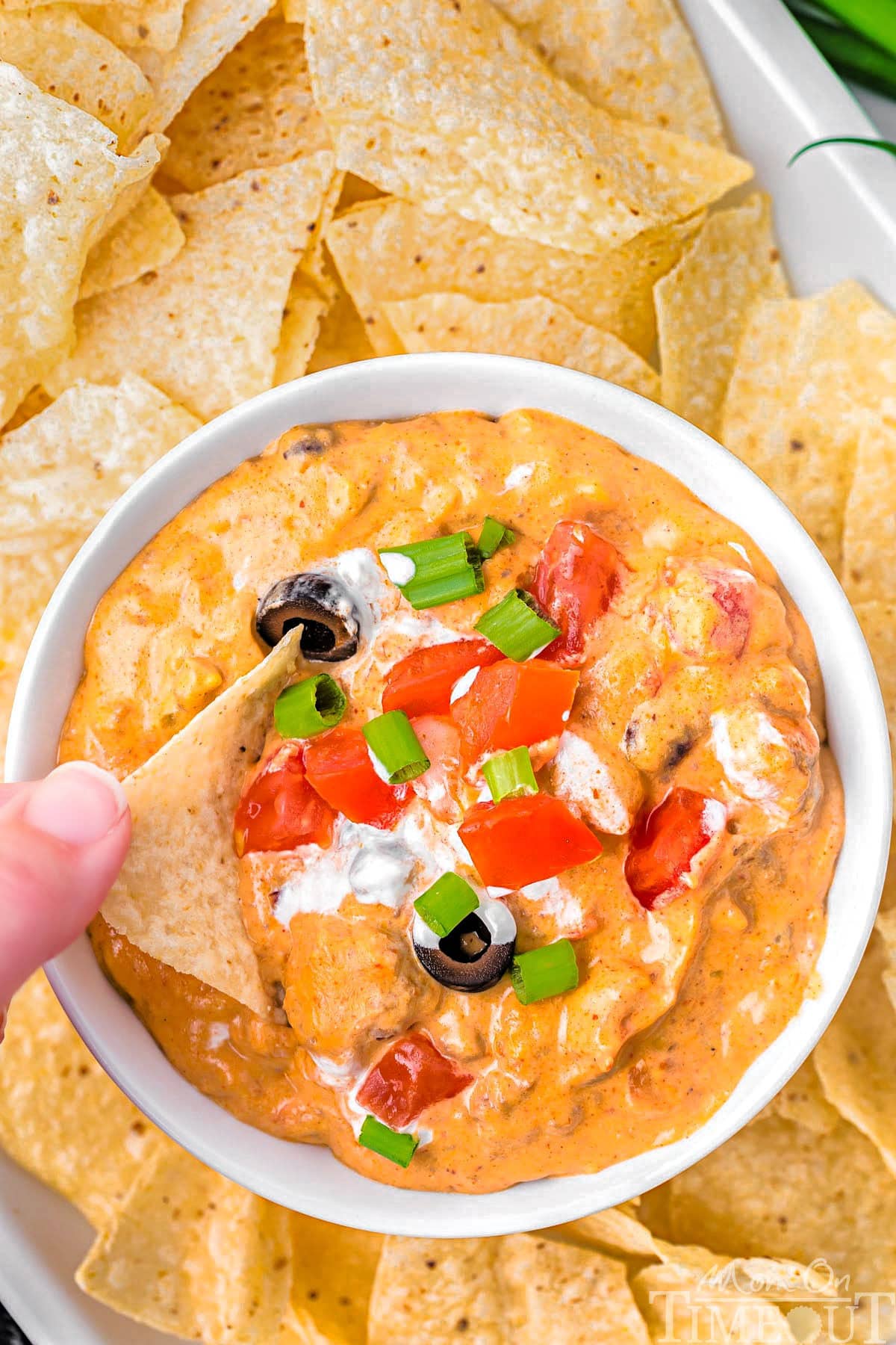 A top down shot of a bowl of crockpot taco dip with a hand dipping a chip into it.