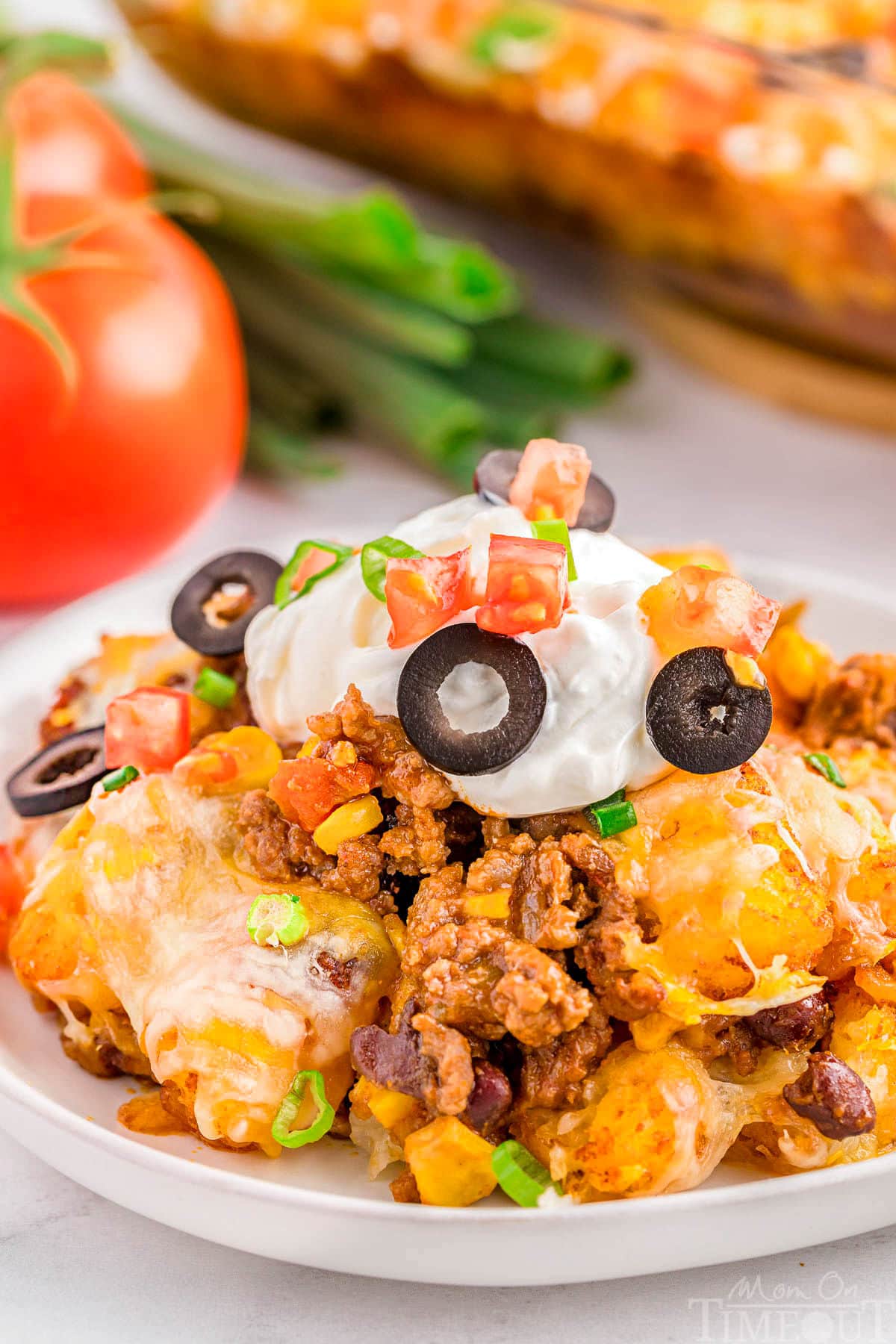 A serving of Mexican tater tot casserole on a white plate topped with sour cream and black olives.