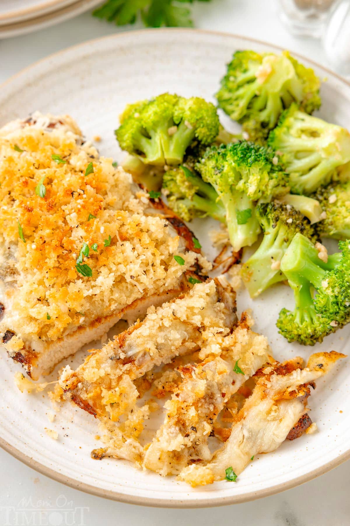 Longhorn Parmesan crusted chicken on a white plate next to a side of broccoli.