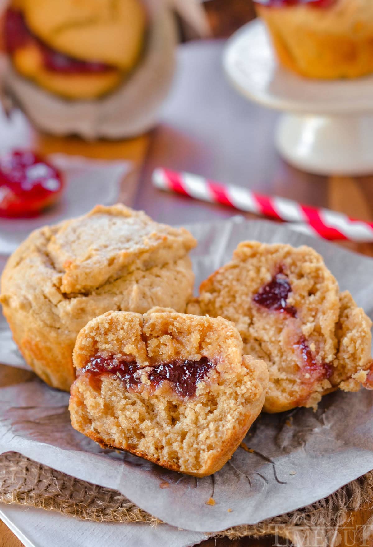 Two peanut butter and jelly muffins on a piece of parchment. One muffin has been split in half to reveal the jelly center.