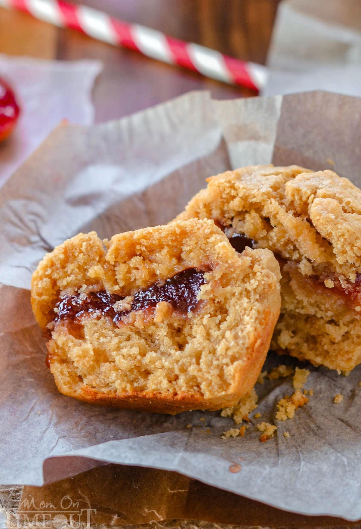 One peanut butter and jelly muffins on a piece of parchment. The muffin has been split in half to reveal the jelly center.