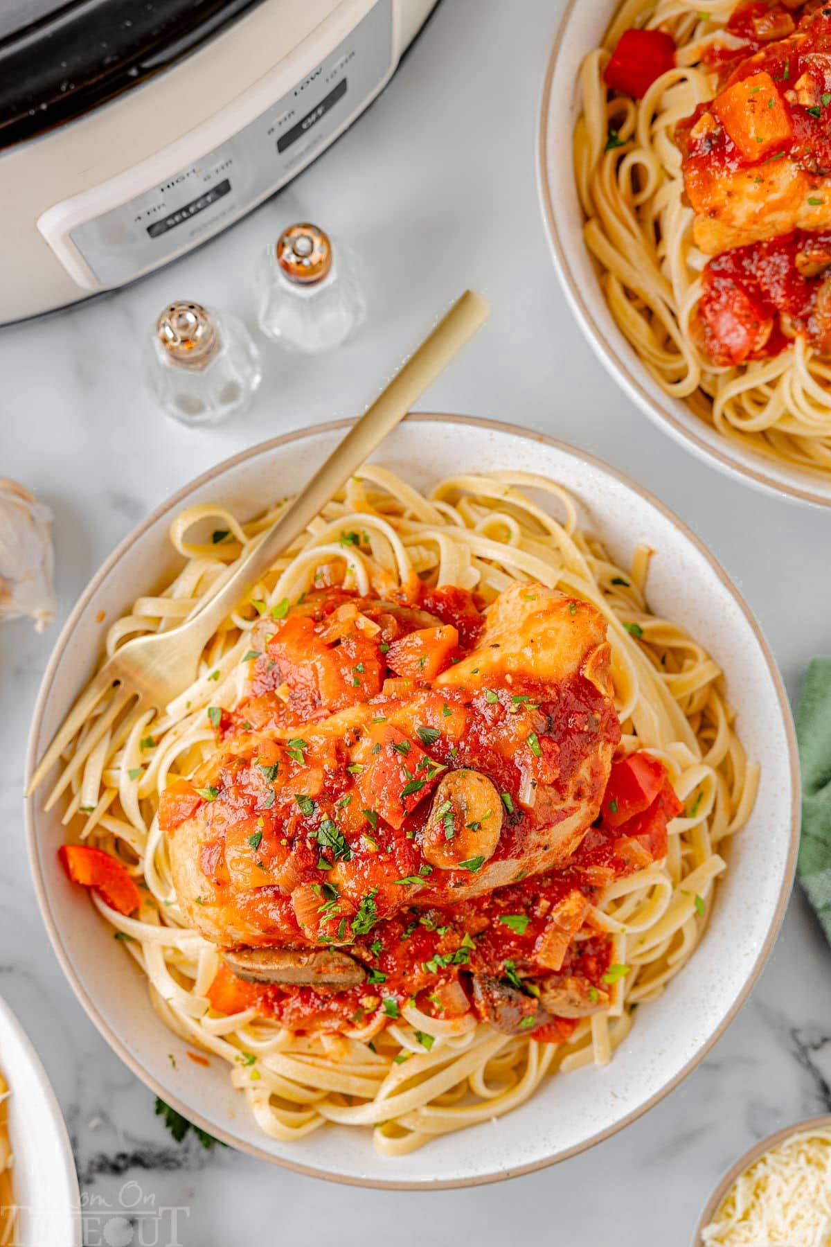 Slow Cooker Chicken Cacciatore on a bed of pasta on a white plate next to a white slow cooker.