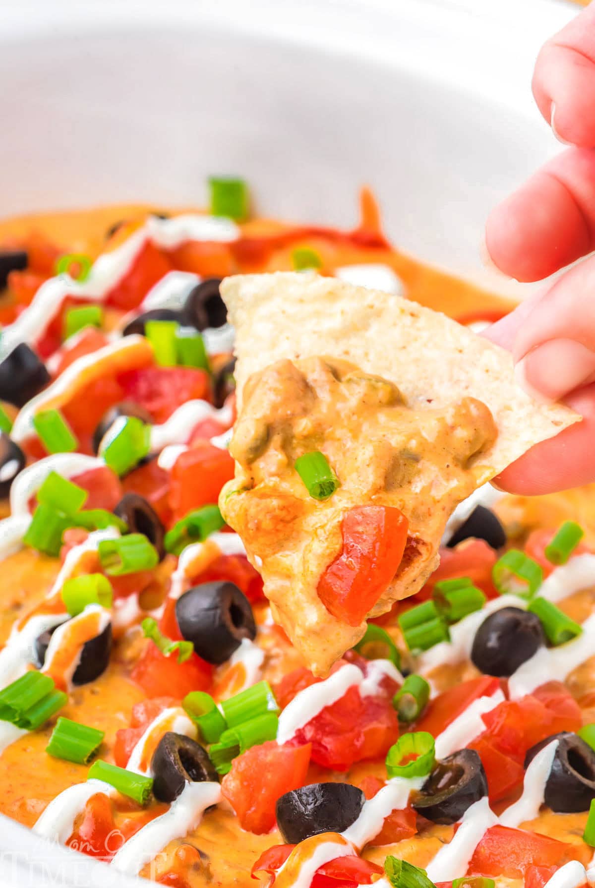 A hand holding up a tortilla chip with crockpot taco dip on it.