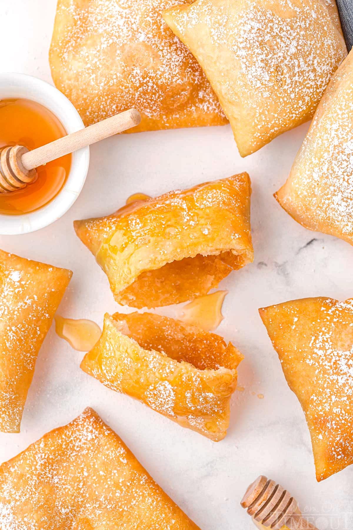 A sopapilla torn in half with additional sopapillas around it on a white surface.