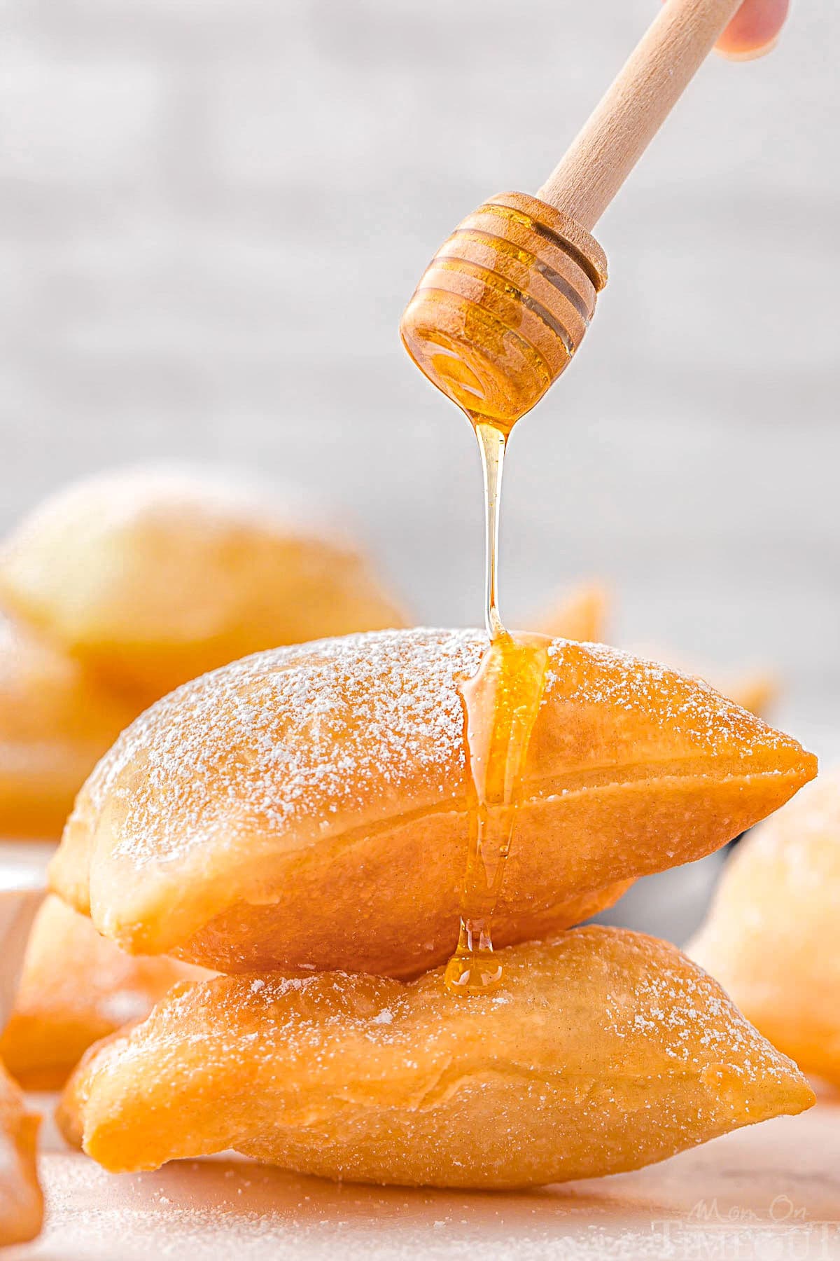 A stack of sopapillas with a honey dipper drizzling honey on top.