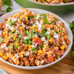 angled view of bowl filled with taco pasta and green skillet in the background with the rest of the taco pasta recipe.