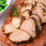 Air fryer pork tenderloin cut into pieces on a wood cutting board with air fryer in background.