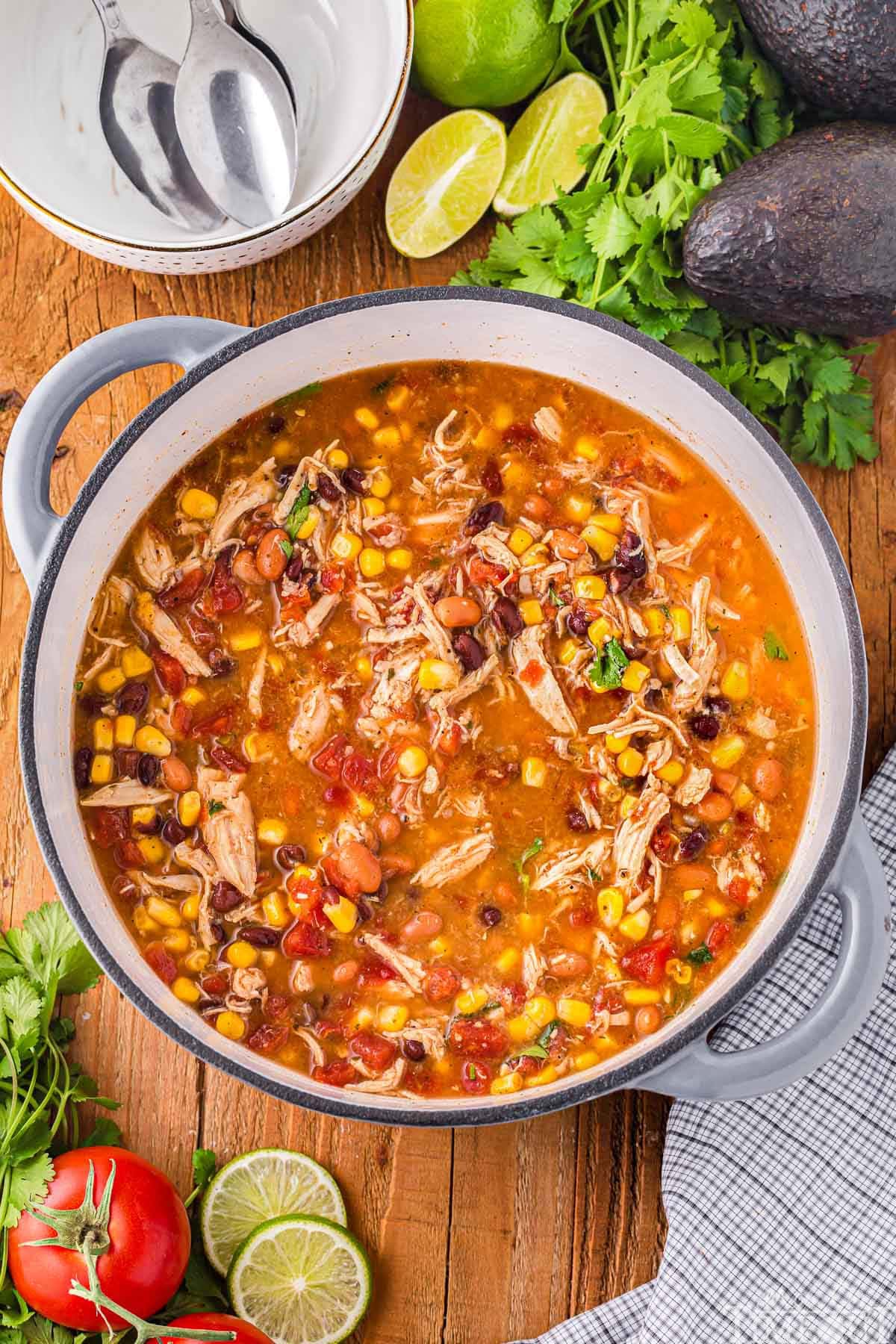 A top down shot of chicken taco soup in a dutch oven with garnishes and bowls on the table next to it.