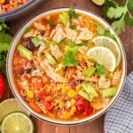 A top down shot of chicken taco soup in a bowl with lime slices next to the bowl.