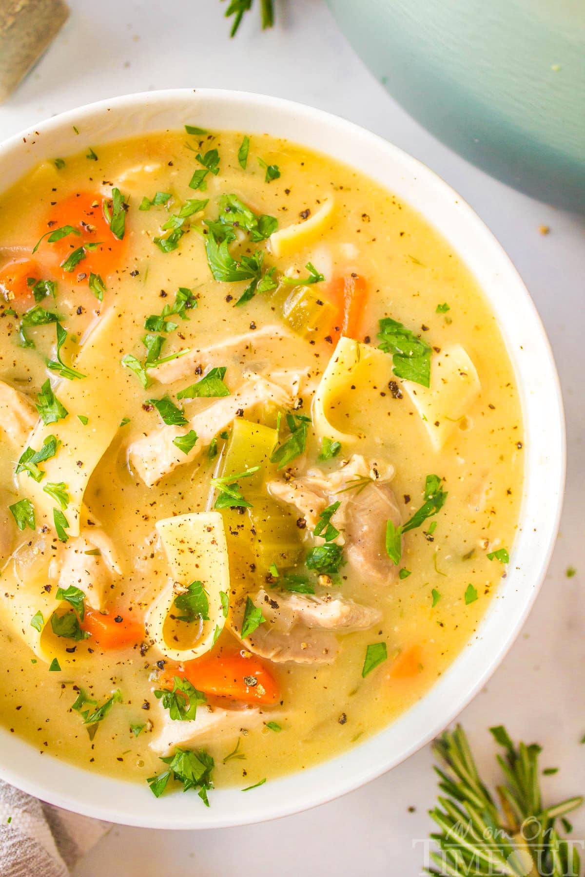 A top down close up shot of a white bowl of creamy chicken noodle soup.