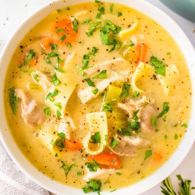 A top down shot of a white bowl of creamy chicken noodle soup garnished with fresh parsley.