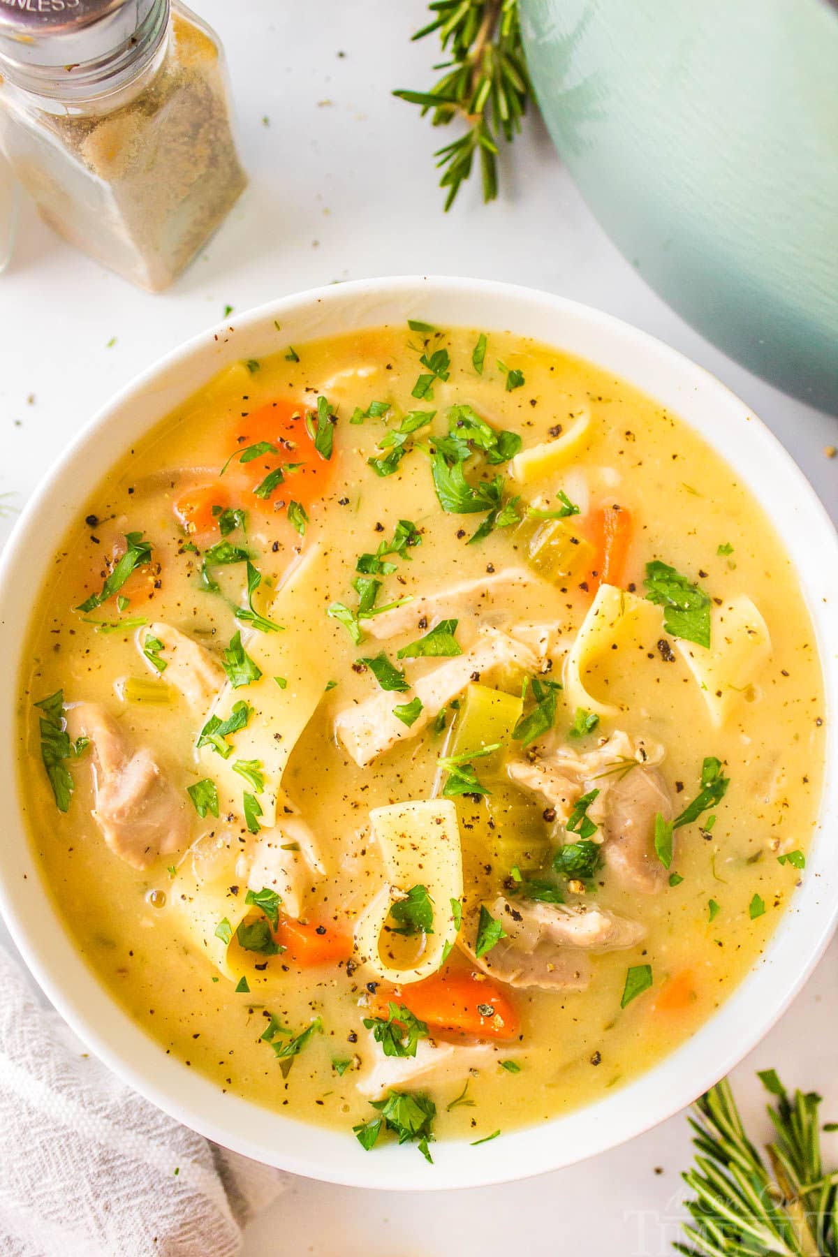 A top down shot of a white bowl of creamy chicken noodle soup.