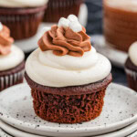 A hot chocolate cupcake on a stack of white plates with more cupcakes in the background.