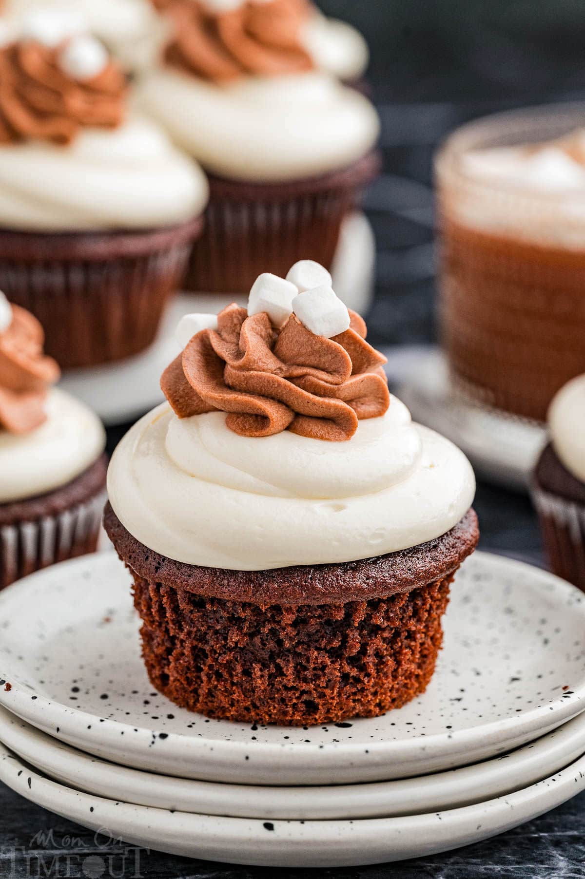 A hot chocolate cupcake on a stack of white plates with more cupcakes in the background.