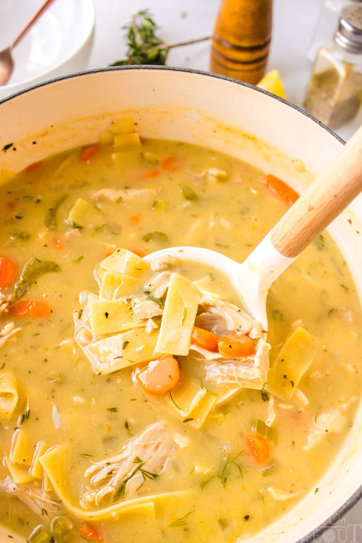 A serving spoon in a pot of chicken noodle soup.