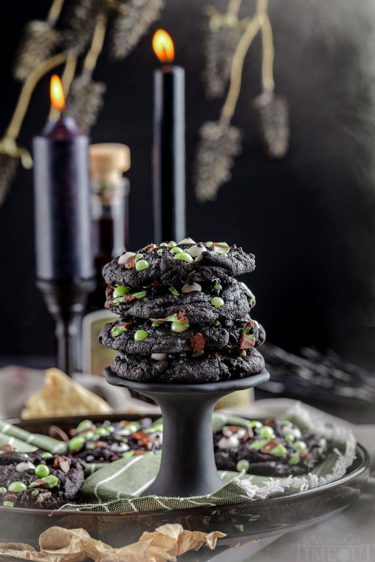 A stack of Halloween monster cookies on a black stand. Black candles and branches are in the background.