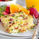 Serving of hash brown breakfast casserole on white round plate with fresh orange wedge and strawberries behind it.