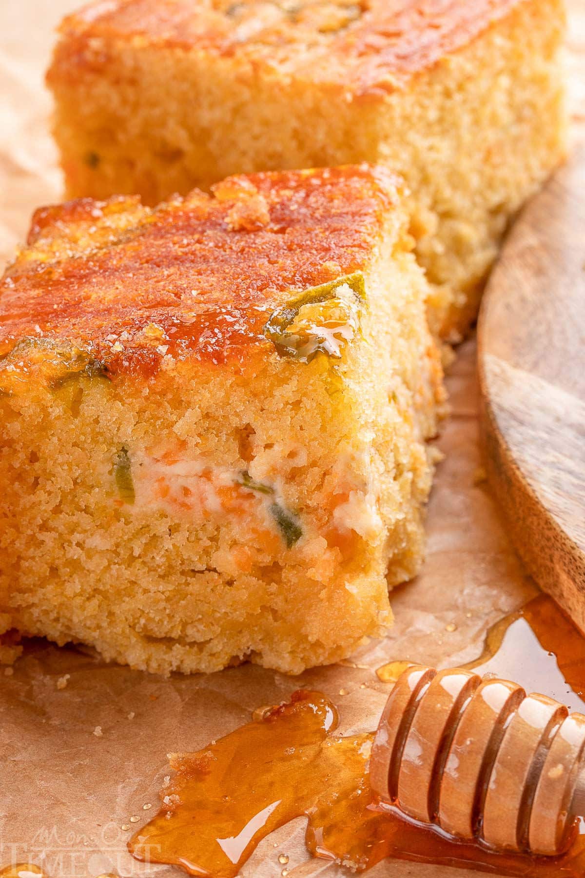 Close look at jalapeno cornbread next to a wand of honey. The jalapeno popper layer in the center is clearly visible in the piece of cornbread.