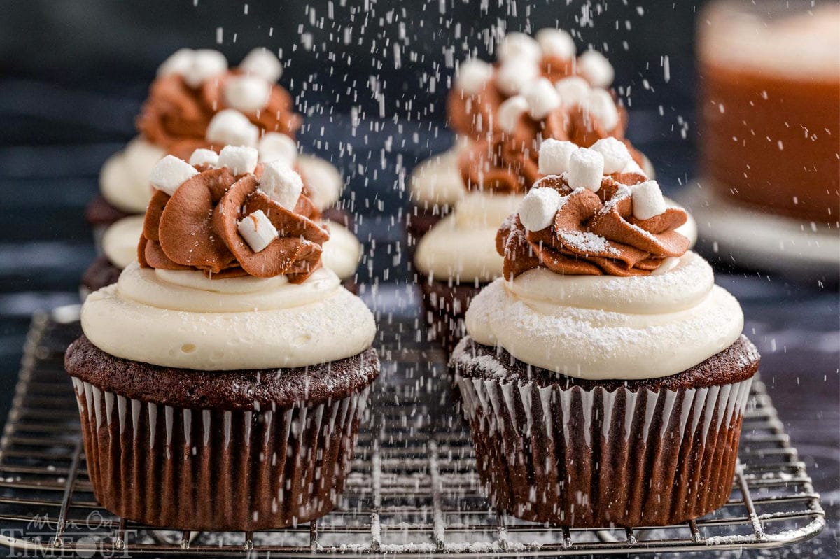 Hot chocolate cupcakes on a metal cooling rack. powdered sugar is dusting the cupcakes from above.