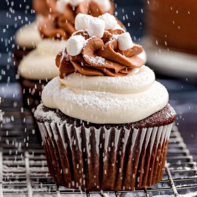 Hot chocolate cupcakes on a metal cooling rack. powdered sugar is dusting the cupcakes from above.