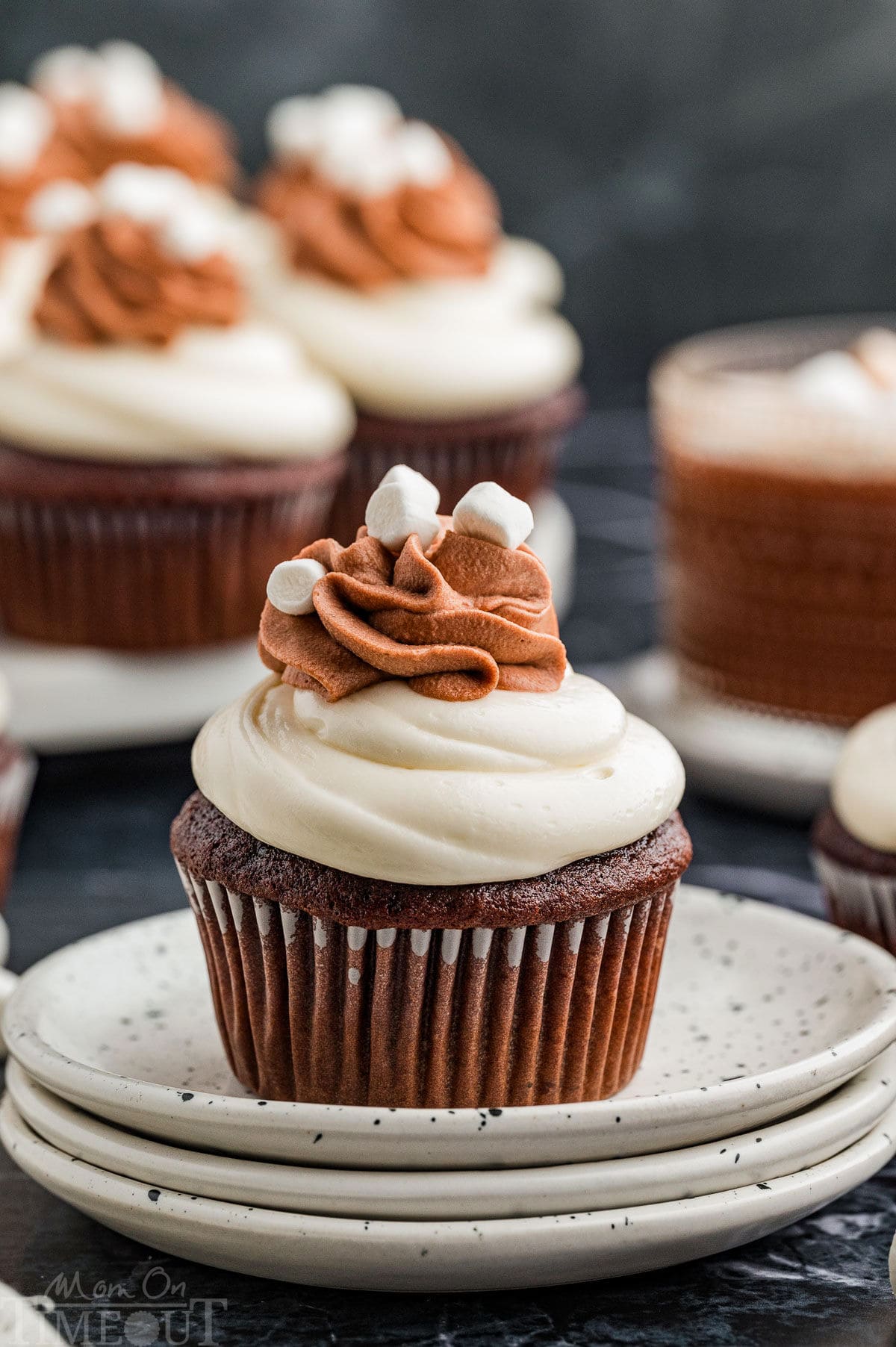 A hot chocolate cupcake on a stack of white plates with more cupcakes in the background.